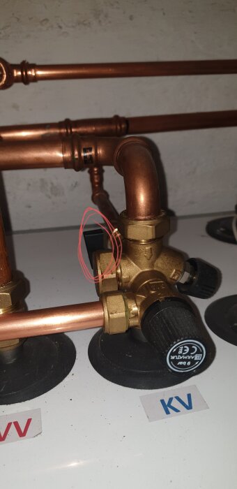 Kopparledningar, mässingsventil, svart knopp, etiketter "KV", "VV", cirkulationspump, teknisk installation, vägg, rörmokeri.