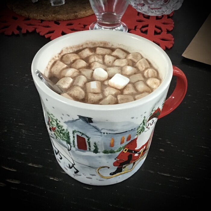 Julmugg full med varm choklad och marshmallows, står på mörkt bord med juldekorationer.