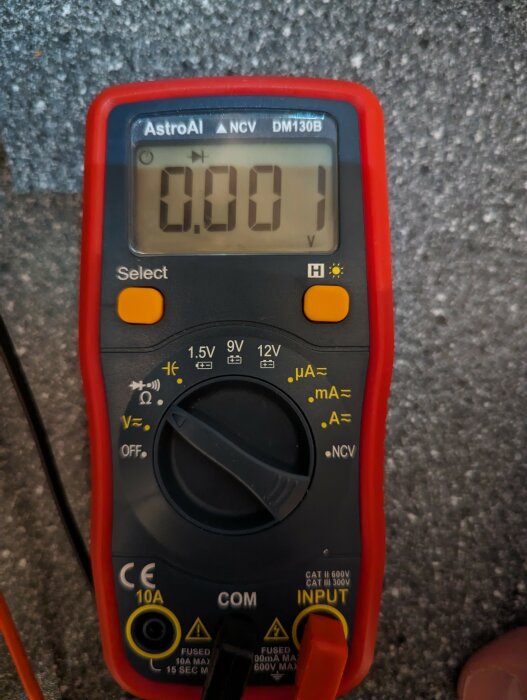 Digital multimeter visar 0.001 volt, hand håller instrumentet, svart-röd design.