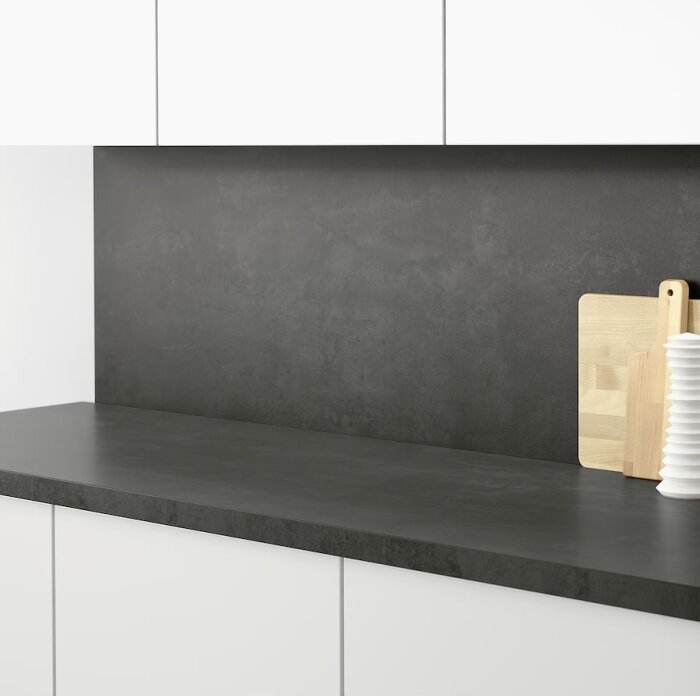 Minimalistiskt kök, mörk arbetsbänk, skärbrädor, vita skåp, enkel design.