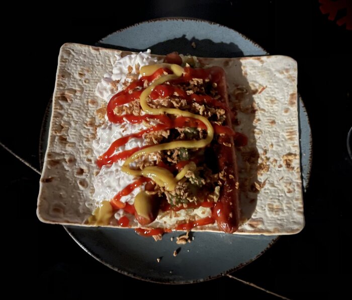 Ett tortillabröd med hackat kött, ost, senap, ketchup, jalapeños, omgiven av vit sås.