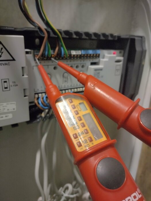 Mätning av elektrisk spänning på en elektrisk panel med en digital multimeter, säkerhetstester i arbetsmiljö.