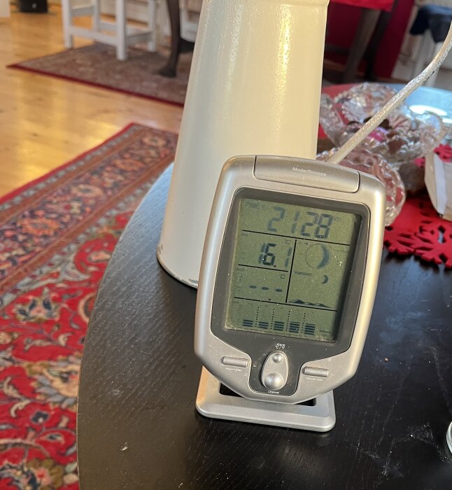 Digital termometer visar inomhustemperatur 21.8 °C och utomhustemperatur 5.6 °C mot bakgrund av hemmiljö.