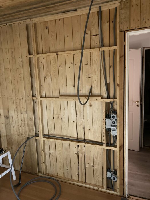 Ett rum under renovering med träpaneler, ledningar och en elektrisk installation synlig.