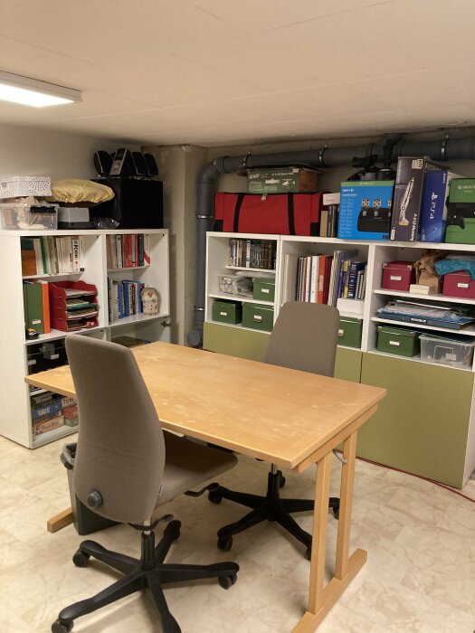 Hemmakontor med skrivbord, stol, hyllor, böcker och organisatoriska lådor i källarmiljö.