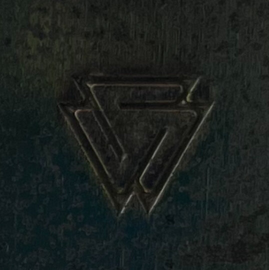 Mörk, stiliserad, metallisk "W" logotyp på mörk texturerad bakgrund.