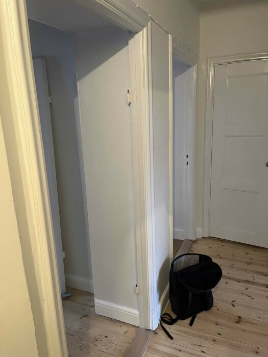 Ett hörn i ett rum med öppna vita garderober och en svart väska på golvet.