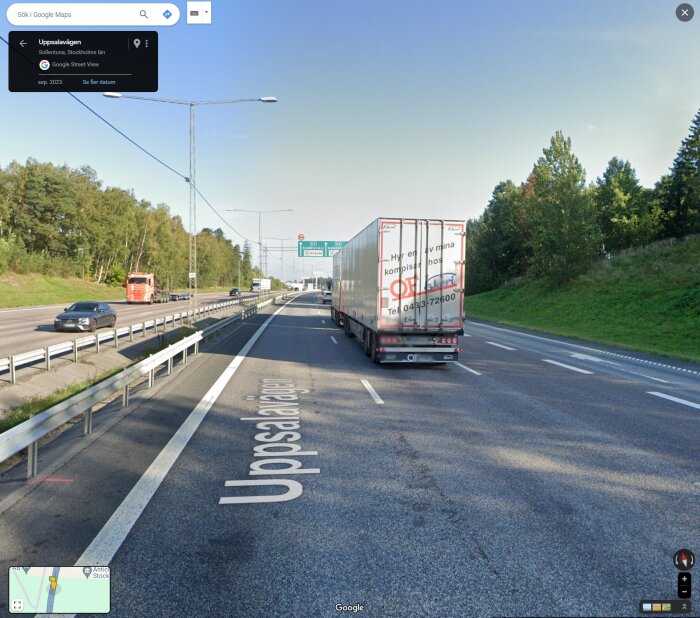 Motorväg med lastbilar, personbil, avfartsskyltar, grönska, klar himmel. Google Street View-vattenmärke.
