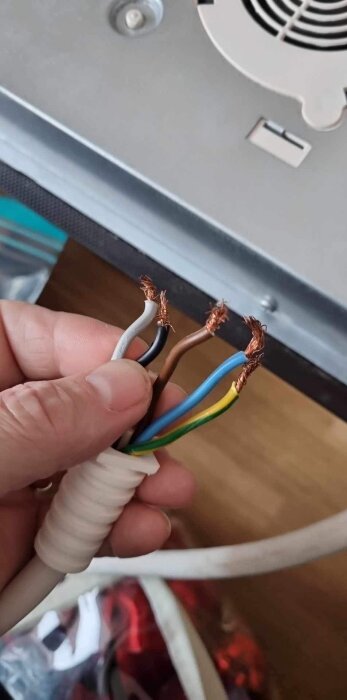 En hand håller ett avskalat elektriskt kabel med exponerade koppartrådar av olika färger.