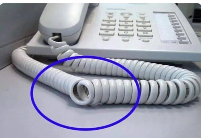 Telefon med snurrad sladd, markerad med blå cirkel, på ett kontor.