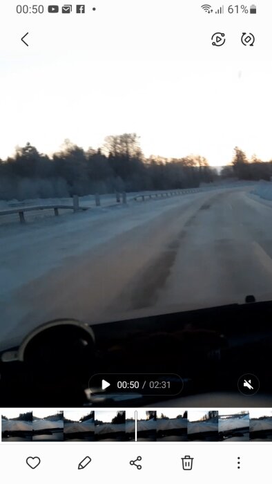 Ett vinterlandskap fångat från bil, gryning eller skymning, tom landsväg, snö på sidorna, skärmbild av videospelare.
