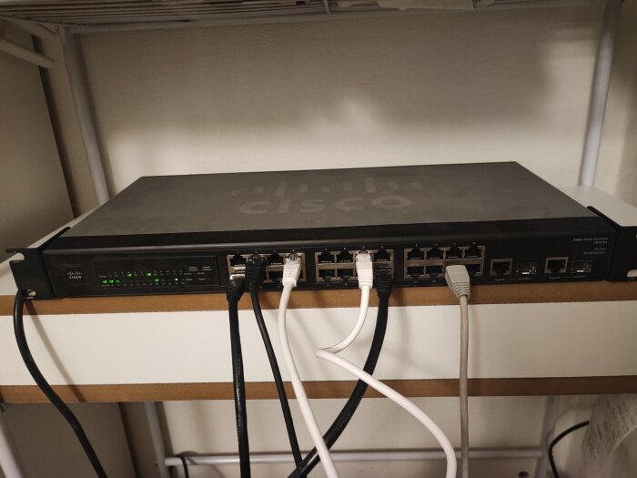 Cisco-switch, nätverksutrustning, kablar anslutna, grön lysdiod, datakommunikation, monterad på hylla.