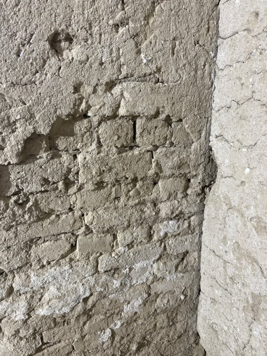 Texturerad vägg med slitage och nedbrytning, exponerade stenar och ojämn yta, tecken på åldring eller förfall.