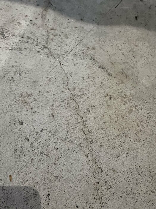 En sprucken, fläckig betonggolv yta med smuts och skuggor.