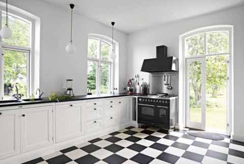 Modernt kök med svartvitt schackrutigt golv, vita skåp, och fönster som ser ut mot trädgården.