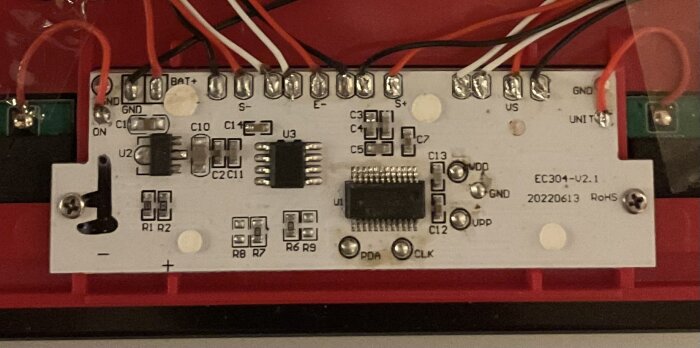 Kretskort med elektronikkomponenter inklusive mikrochip, kondensatorer och lödda anslutningar, monterat på röd bas.