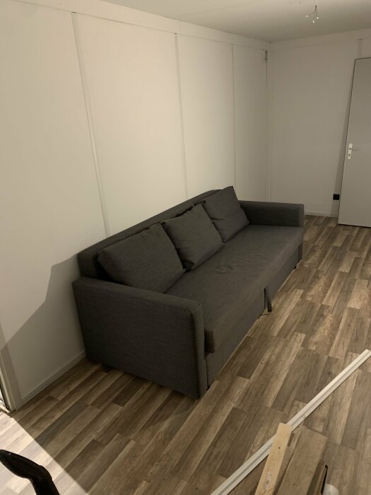 Modernt minimalistiskt vardagsrum med grå soffa, trägolv, vita väggar och osammanhängande möbelbygge.