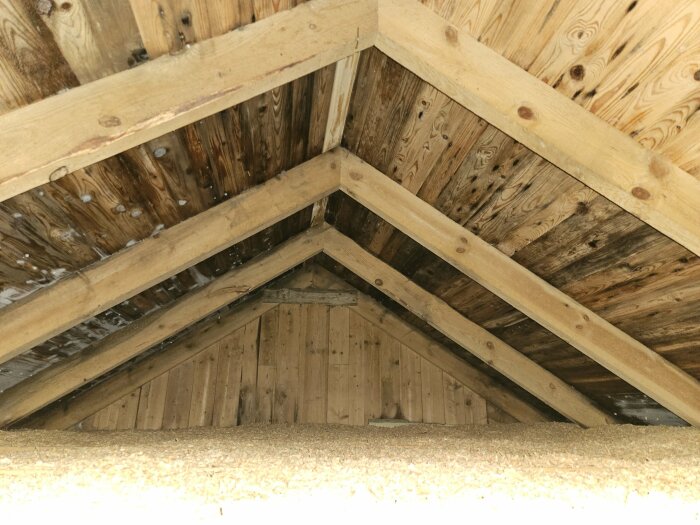 Träkonstruktion av takstol i vinklat loft, med synliga spikar och isoleringsmaterial på golvet.