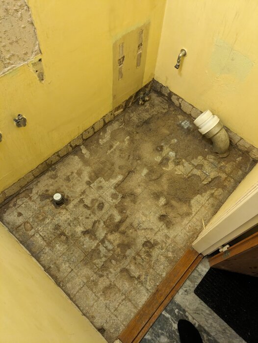 Renoveringsbehov i badrum, gamla kakel och rör synliga, slitna ytor, slitet golv, ofärdig vägg.