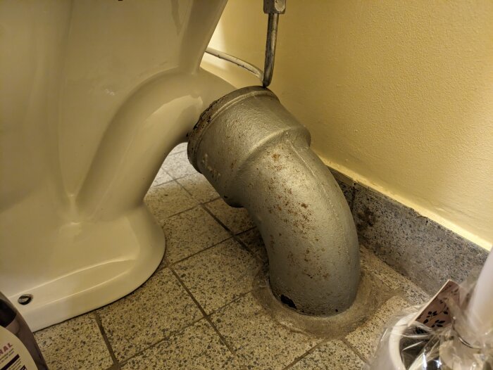 Ett toalettstol ansluten till en grov avloppsrör i ett kaklat badrum.