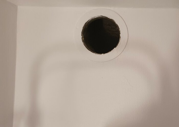 Cirkulärt hål i en vit vägg med mörkt inre och synliga spår av reparation.