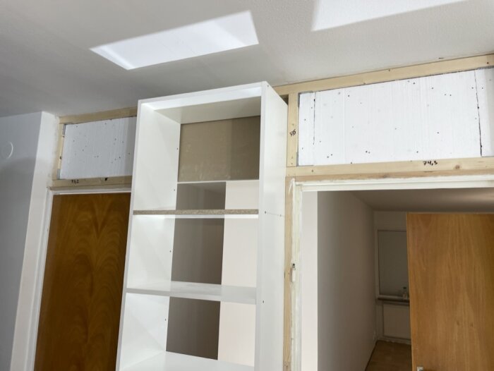 Renovering pågår, vit bokhylla, trästommar, oavslutat utrymme, innerdörr, ljusinläpp från taket.