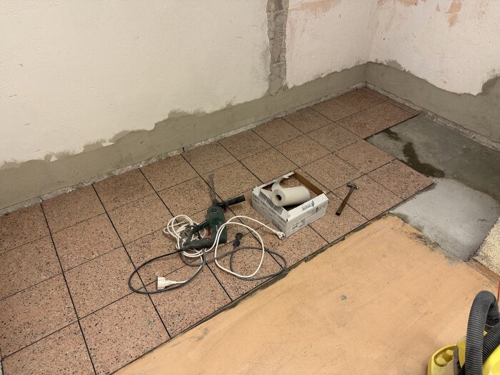 Renoveringsplats, verktyg och byggmaterial på ett kaklat golv, oslipad vägg, vattenskada eller läckage.