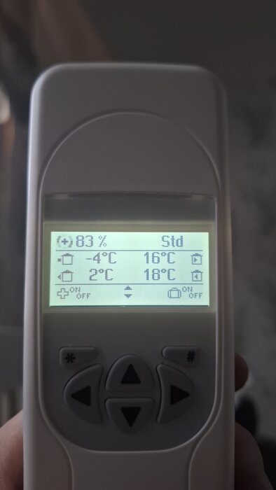 Digital termostat visar rumstemperaturer och inställningar, fyra knappar nedanför LCD-skärmen, hand håller enheten.