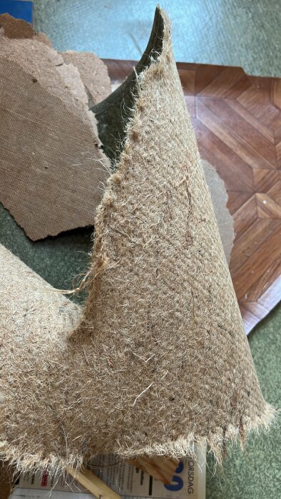 Delvis söndersliten kartong med kattklösmöbel i grov textil nära trägolv och tidning.