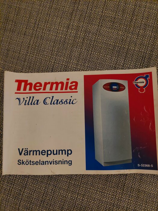 Manual för Thermia Villa Classic värmepump, skötselanvisning, ligger på texturerad yta.