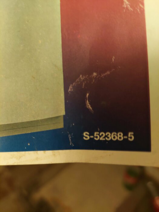 Suddig bild, pappershörn, text "S-52368-5", delvis täckt, mörk bakgrund med röda toner.