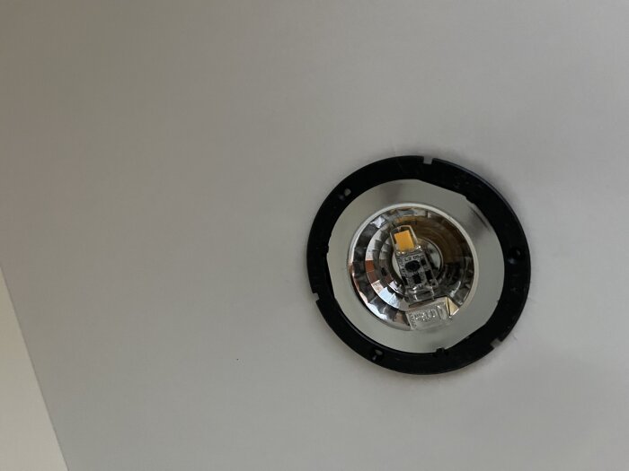 Takmonterad LED-spotlight utan kåpa, exponerad ljuskälla, reflektor, vita kabelanslutningar, väntar på underhåll eller installation.