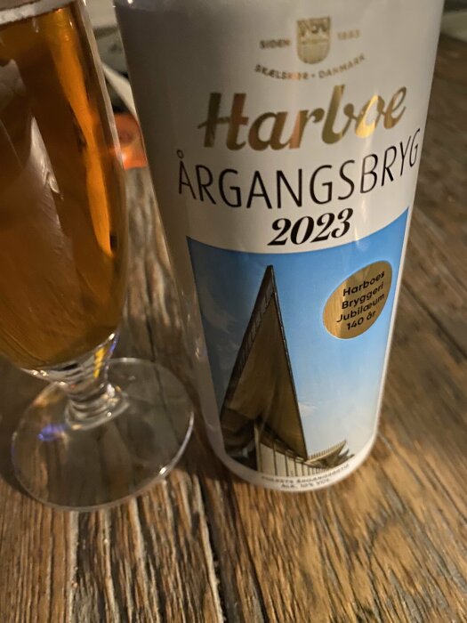 En ölflaska från Harboe med texten "Årgangsbrygg 2023" och ett glas på ett träbord.