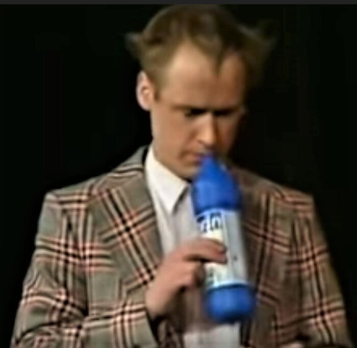 En man i rutig kavaj luktar på en stor blå flaska.