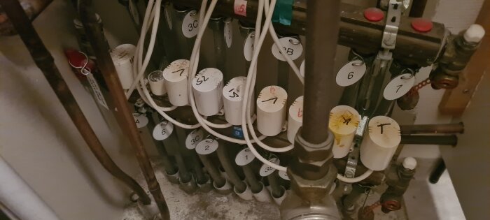 Värmerör med etiketterade ventiler och kablar i rörskåp.