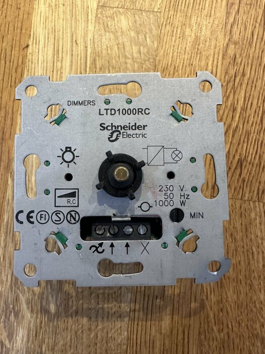 Elektronisk dimmerkomponent från Schneider Electric på träbakgrund; reglage och terminaler synliga.