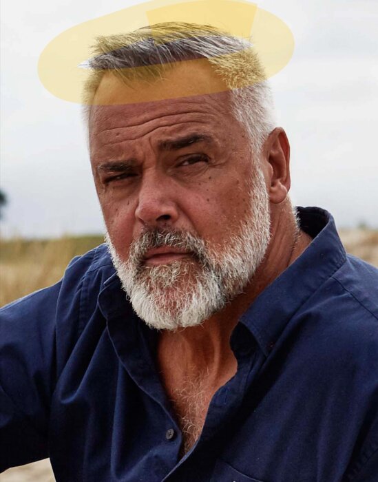 Äldre man, gråskägg, blå skjorta, seriös blick, fotoshoppat guldhjärta ovanför huvudet.