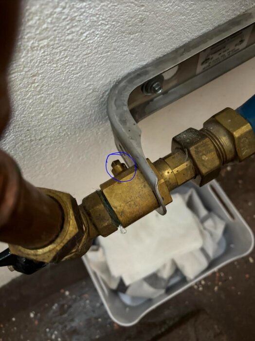 Mässingsrör med vattenläcka, markerad med blå cirkel, över en vit behållare, närbild.