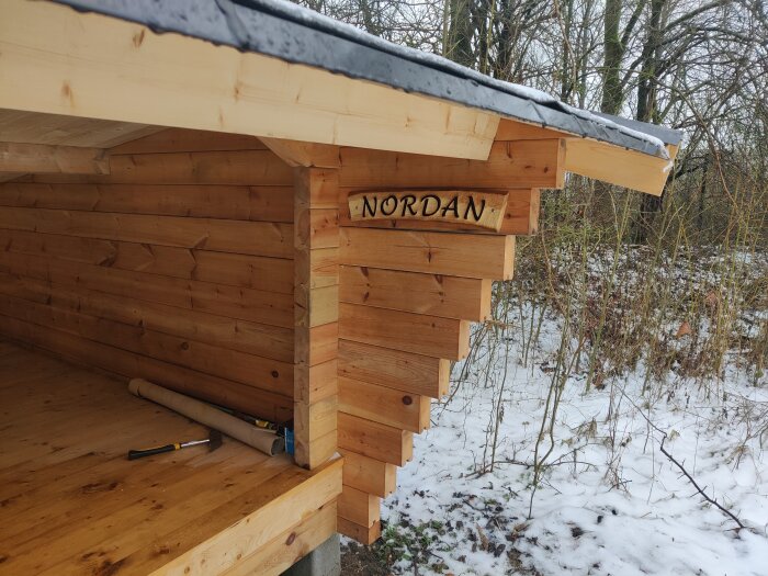 Träkonstruktion i snöigt landskap, skylt med "NORDAN", verktyg på bänk, vinterväder, naturen.