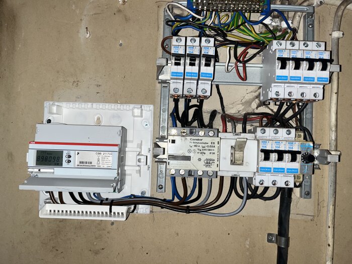 Elektrisk fördelningstavla med säkringsautomater, energimätare och säkerhetsbrytare på en betongvägg.