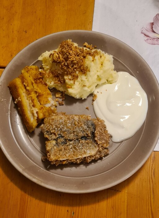 Tallrik med varierad mat, panerad fisk, mosad potatis med topping, friterade strimlor, klick av sås, hemmiljö.