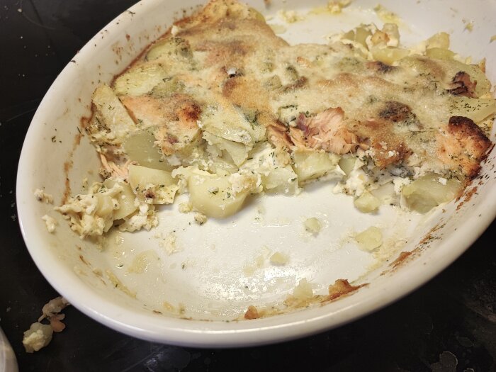 Delvis uppäten gratäng med potatis och lax i vit form. Restmat, kvar på disk.
