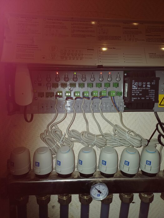 Uppvärmingssystemskontrollpanel med termostater, ledningar, instruktionsdekal och manometer.
