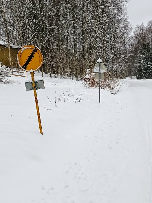 Vinterväg med snö, trafikskyltar, träd, och fotspår. No entry och byvägsskyltar synliga.