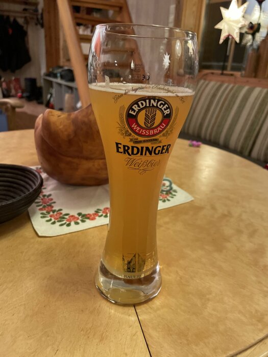 Ett glas Erdinger Weissbier på ett träbord; inomhusmiljö, mysig atmosfär.