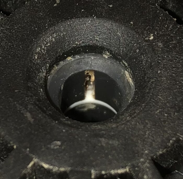 Närbild av ett svart gummiobjekt med yttre textur och cirkulär öppning i mitten, smutsiga detaljer, oskarpt djup.