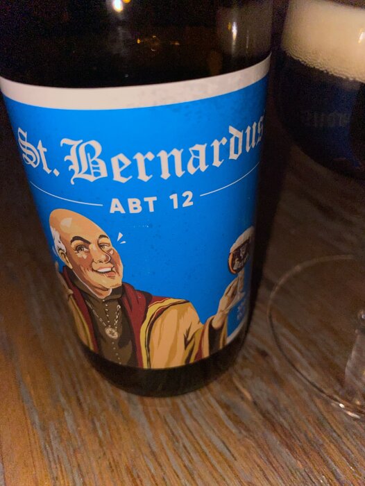 Flaska med etikett "St. Bernardus Abt 12", stiliserad munk, mörkt öl i glas i bakgrunden.