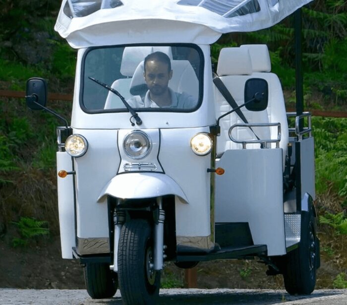 Man kör en vit trehjulig skoter med tak. Utomhus, dagtid, koncentrerad blick.