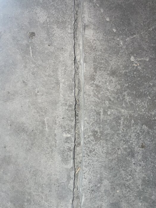 Grå betonggolv med en lång, tunn spricka och en ledningskanal eller fog.