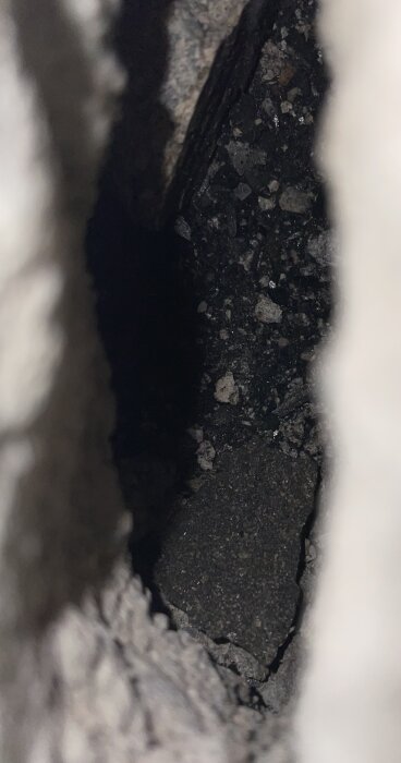 Bild av en mörk spricka eller hålighet, antagligen i mark eller sten, med ojämn textur.